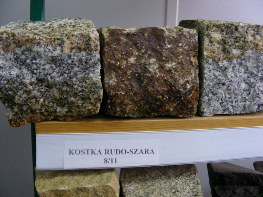 Przykładowe kostki z granitu w odcieniach szarości i brązu, ułożone na drewnianej półce, z widoczną etykietą 'KOSTKA RUDO-SZARA 8/11'.